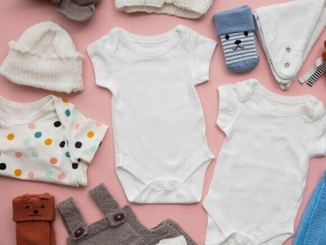Roupas de bebê diversas, dispostas sobre uma superfície rosa. Roupas de bebê diversas, dispostas sobre uma superfície rosa.