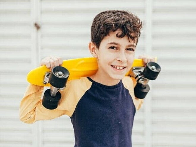 Menino sorrindo e segurando um skate pequeno em cima dos ombros Menino sorrindo e segurando um skate pequeno em cima dos ombros
