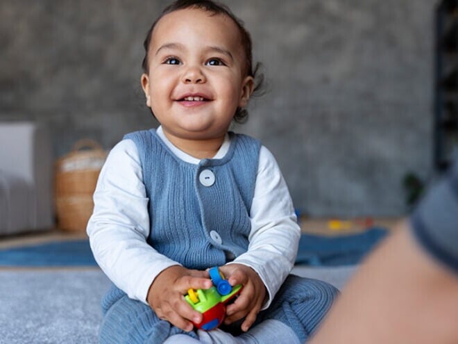 Bebê de aproximadamente 1 ano sentado no tapete da sala segurando brinquedos. Bebê de aproximadamente 1 ano sentado no tapete da sala segurando brinquedos.