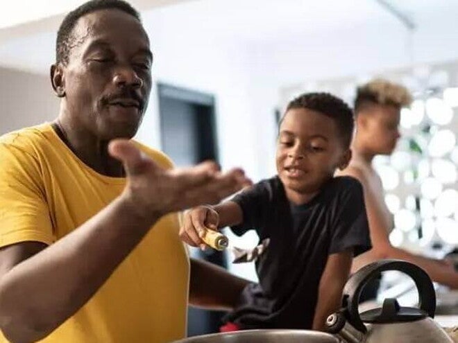 ser pai Pai e filho cozinham juntos como uma homenagem de dia dos pais. O pai está mexendo uma panela e o filho, ao seu lado, o ajuda.