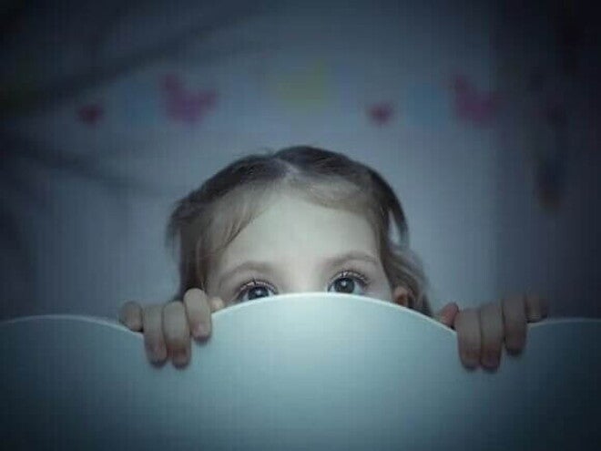 Sonambulismo infantil criança se esconde atrás de cabeceira de cama em quarto infantil, rosto com expressão assustada.