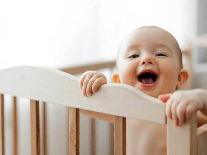 Bebê de 6 meses parado em seu berço se segurando na grade. 
