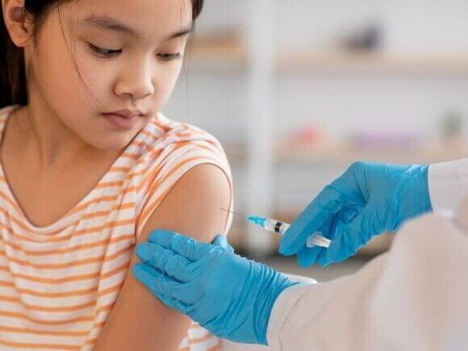 Uma criança recebendo uma injeção no braço de um profissional de saúde usando luvas azuis, simbolizando a aplicação da vacina HPV.