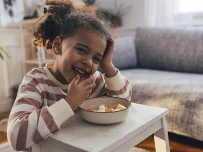 Foto de uma criança fazendo um lanche e comendo com as mãos uma vasilha de salada de frutas, um exemplo de alimento rico em vitamina C Foto de uma criança fazendo um lanche e comendo com as mãos uma vasilha de salada de frutas, um exemplo de alimento rico em vitamina C