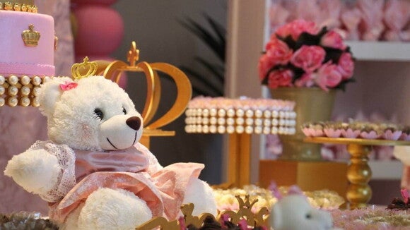 Um urso de pelúcia branco com uma coroa dourada e vestido rosa sentado em uma mesa de sobremesas em uma festa de chá de bebê. Um urso de pelúcia branco com uma coroa dourada e vestido rosa sentado em uma mesa de sobremesas em uma festa de chá de bebê.