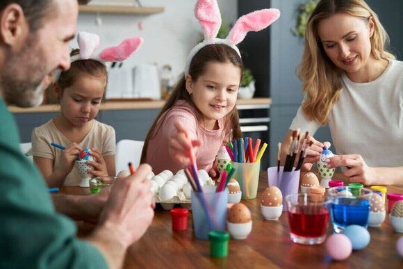 Família feliz de quatro pessoas decorando ovos de Páscoa em casa.