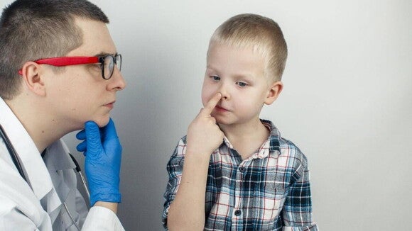 Médica examinando a garganta de um menino pequeno com a língua para fora, em consulta para diagnosticar ou avaliar sintomas de adenoide aumentada.