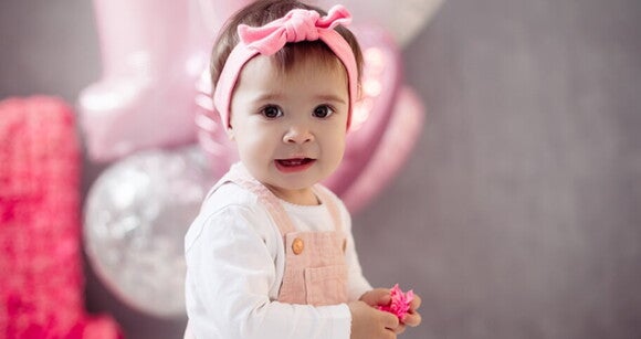 Bebê usando macacão e laço na cabeça sorrindo. Bebê usando macacão e laço na cabeça sorrindo.