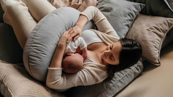 Mulher amamentando bebê que está acomodado em uma almofada de amamentação. Mulher amamentando bebê que está acomodado em uma almofada de amamentação.