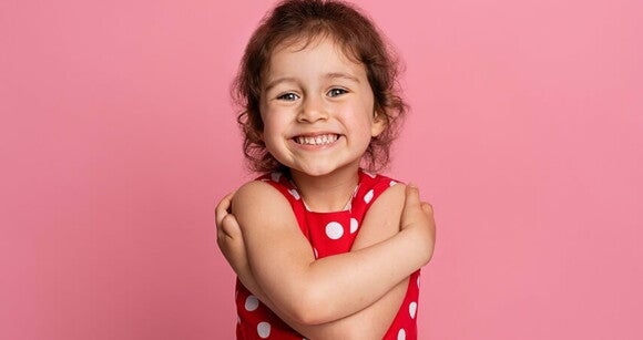 Menina usando roupa vermelha com bolinhas brancas sorrindo em frente a um fundo cor de rosa Menina usando roupa vermelha com bolinhas brancas sorrindo em frente a um fundo cor de rosa