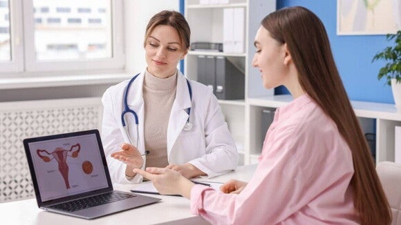Uma mulher em consulta médica com sua ginecologista, que aponta para uma ilustração do útero e ovários em uma tela de laptop, discutindo opções de planejamento familiar e contracepção.
