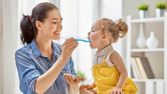 Mãe sorridente alimentando sua filha pequena com uma colher.