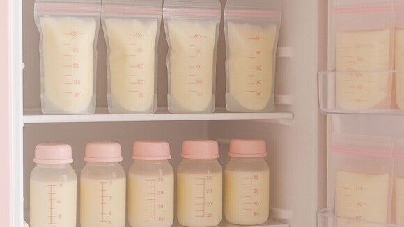 Leite materno congelado e acondicionado em bolsas plásticas e pequenos frascos com tampas rosas, organizados nas prateleiras de um freezer ou refrigerador.