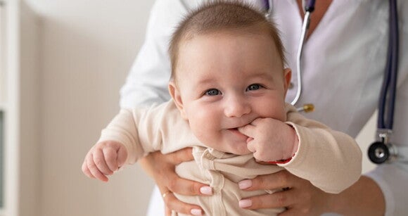 Bebê sorrindo com dedinhos na boca no colo de uma médica Bebê sorrindo com dedinhos na boca no colo de uma médica