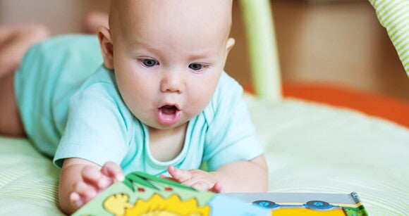 Bebê de bruços tentando pegar um livrinho que está na sua frente