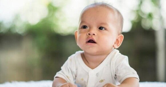 Bebê com macacão branco olhando atentamente com a boca aberta Bebê com macacão branco olhando atentamente com a boca aberta