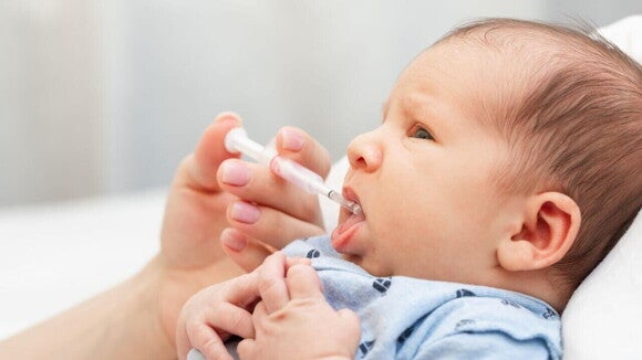 Um bebê deitado, com a boca aberta, recebendo uma medicação na boca através de uma seringa