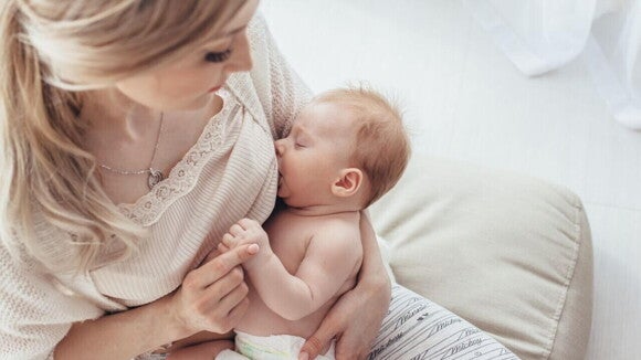 Vista de cima de uma mãe amamentando seu bebê recém-nascido, que está adormecido, representando o período de amamentação.