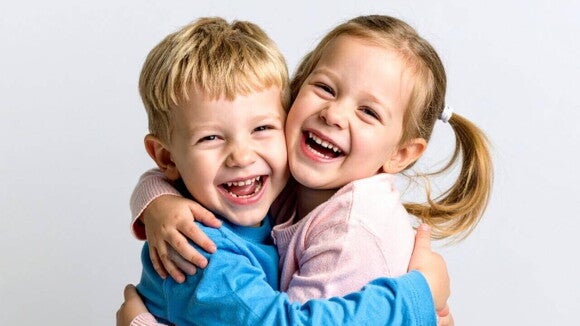 Um menino e uma menina, ambos pequenos, sorrindo e se abraçando carinhosamente.