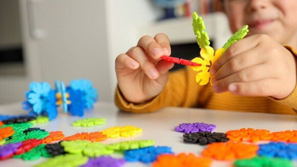 Uma criança sentada em uma mesa com vários brinquedos sensoriais, manipulando um brinquedo de encaixar peças. Uma criança sentada em uma mesa com vários brinquedos sensoriais, manipulando um brinquedo de encaixar peças.