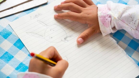 Mãos de uma criança canhota, desenhando com um lápis em uma folha de caderno. Mãos de uma criança canhota, desenhando com um lápis em uma folha de caderno.