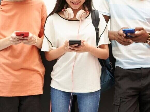 Três jovens em pé, utilizando celulares Três jovens em pé, utilizando celulares