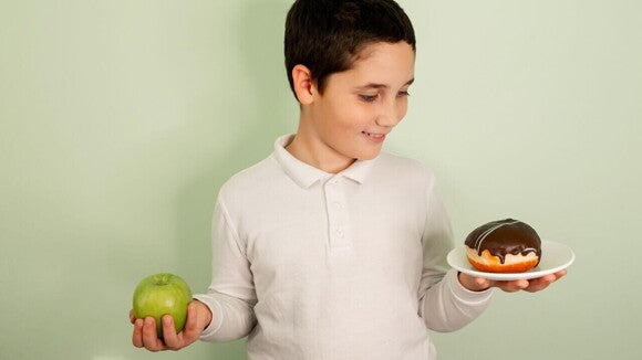 Menino escolhendo entre uma maçã e uma rosquinha, representando as escolhas alimentares e o colesterol infantil Menino escolhendo entre uma maçã e uma rosquinha, representando as escolhas alimentares e o colesterol infantil