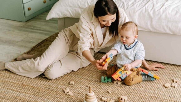 Mãe sentada em um tapete ao lado do bebê com vários brinquedos espalhados Mãe sentada em um tapete ao lado do bebê com vários brinquedos espalhados