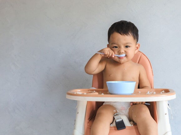Como saber se meu bebê tem intolerância ao glúten? Foto de bebe comendo em cadeira alta.