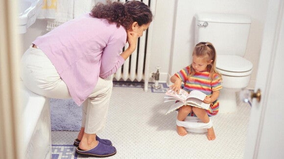 Mãe supervisionando a filha no banheiro durante o processo de desfralde. A imagem ilustra as melhores práticas sobre como tirar a criança da fralda com paciência e apoio.