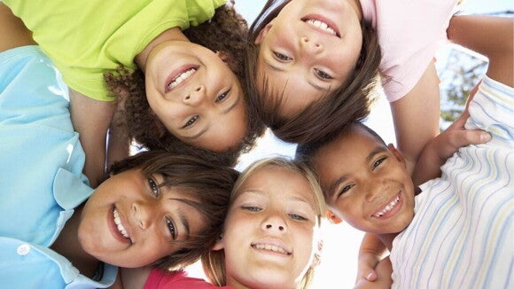 Grupo de cinco crianças sorrindo e abraçadas em círculo, olhando para a câmera. 