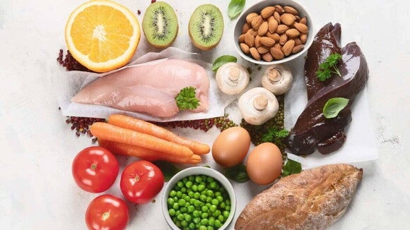 Visão aérea de diversos alimentos ricos em vitaminas do complexo B para crianças, dispostos em uma superfície branca.