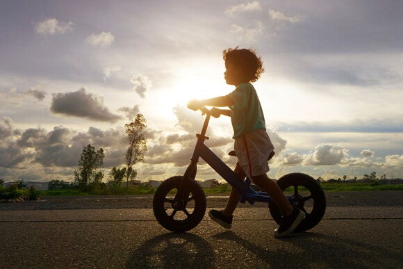Tem uma idade certa para começar a andar de bicicleta? Foto de criança andando de bicicleta usando os pés como apoio.