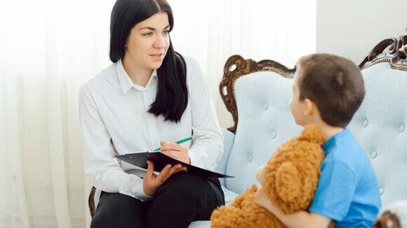 Psicóloga conversa com criança durante sessão terapêutica, em ambiente acolhedor.