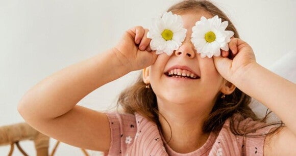 Menina usando camiseta florida rosa sorrindo com flores de margaridas sobre os olhos Menina usando camiseta florida rosa sorrindo com flores de margaridas sobre os olhos