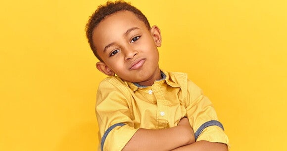 Menino com os braços cruzados vestindo camisa amarela e em um fundo amarelo Menino com os braços cruzados vestindo camisa amarela e em um fundo amarelo