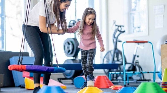 Uma mulher sorrindo e segurando a mão de uma criança, que está andando em um espaço para exercícios infantis. Uma mulher sorrindo e segurando a mão de uma criança, que está andando em um espaço para exercícios infantis.
