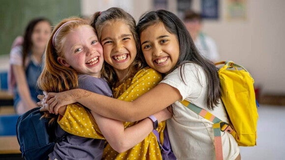 Três meninas abraçadas e sorrindo na sala de aula Três meninas abraçadas e sorrindo na sala de aula