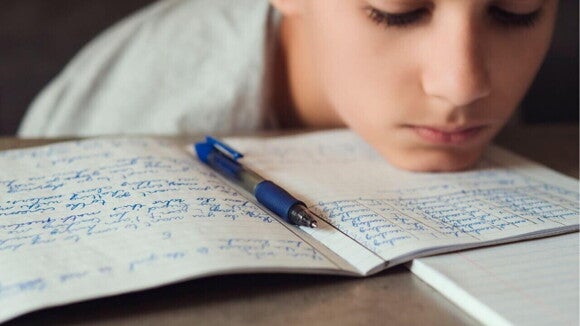 Criança com a cabeça deitada sobre um caderno com aspecto de desânimo Criança com a cabeça deitada sobre um caderno com aspecto de desânimo