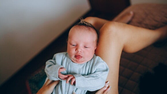 Mãos de um adulto segurando um bebê recém-nascido deitado de costas, com a língua para fora.