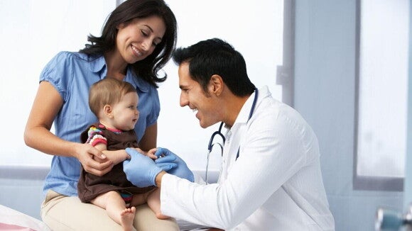 Mulher sorridente segurando um bebê, enquanto um médico examina a criança em um consultório iluminado. Mulher sorridente segurando um bebê, enquanto um médico examina a criança em um consultório iluminado.
