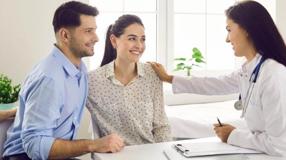 Casal sorridente realizando uma consulta com uma profissional de saúde Casal sorridente realizando uma consulta com uma profissional de saúde