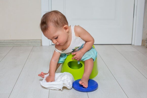 Foto de bebê sentado no penico brincando com uma fralda Foto de bebê sentado no penico brincando com uma fralda