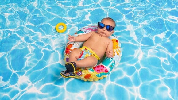 Bebê com oculos escuros deitado em bóia colorida na piscina Bebê com oculos escuros deitado em bóia colorida na piscina