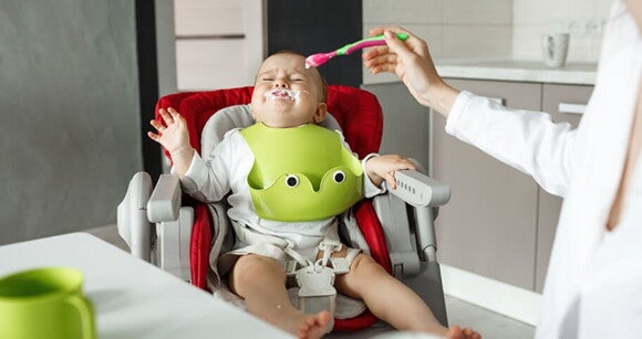Mãe tentando dar papinha para bebê que está na cadeirinha chorando. Mãe tentando dar papinha para bebê que está na cadeirinha chorando.