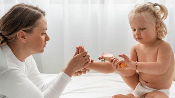 Uma mulher observa o pé de um bebê sentado à sua frente com um brinquedo nas mãos Uma mulher observa o pé de um bebê sentado à sua frente com um brinquedo nas mãos