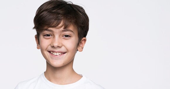 Menino de cabelo liso usando camiseta branca e sorrindo em frente a uma parede branca. Menino de cabelo liso usando camiseta branca e sorrindo em frente a uma parede branca.