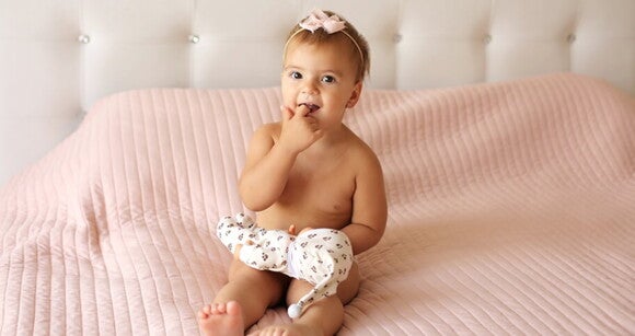 Menina de aproximadamente 1 ano sentada na cama brincando com uma boneca. Menina de aproximadamente 1 ano sentada na cama brincando com uma boneca.