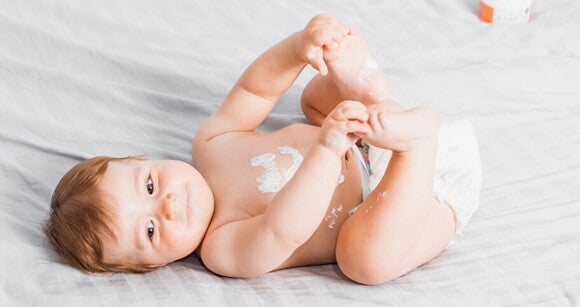 Bebê deitado em uma cama usando fralda e com creme hidratante na barriga Bebê deitado em uma cama usando fralda e com creme hidratante na barriga