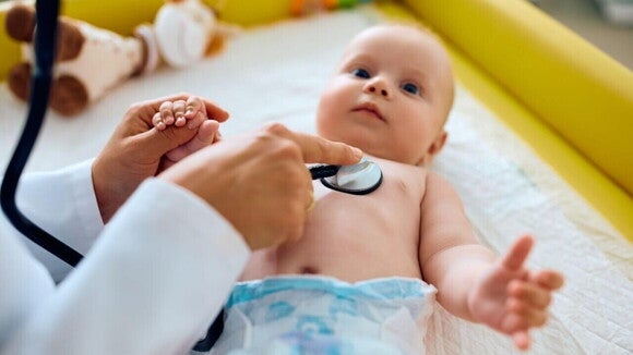 Um bebê deitado, sendo examinado por um profissional de saúde, com um estetoscópio